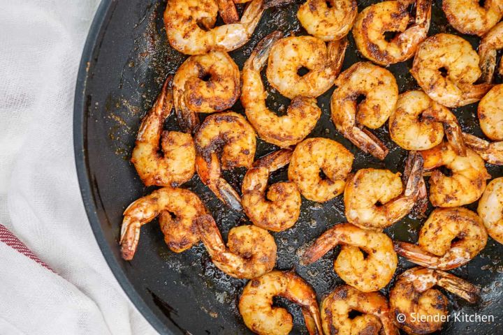 Blackened shrimp with homemade seasoning in a black skillet with butter.