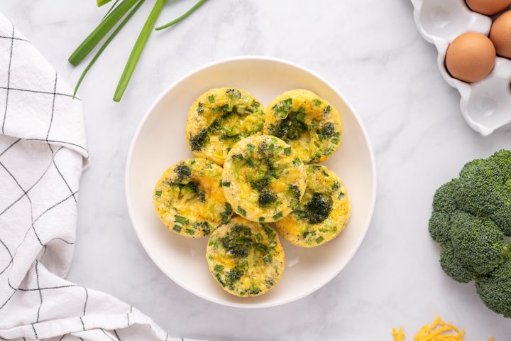 Broccoli Cheddar Egg Muffins with broccoli florets , green onions, and shredded cheese. 