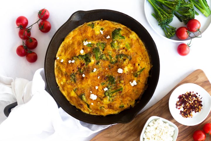 Broccoli and cheese frittata cooked in a skillet with eggs, broccoli, ricotta cheese, and tomatoes.