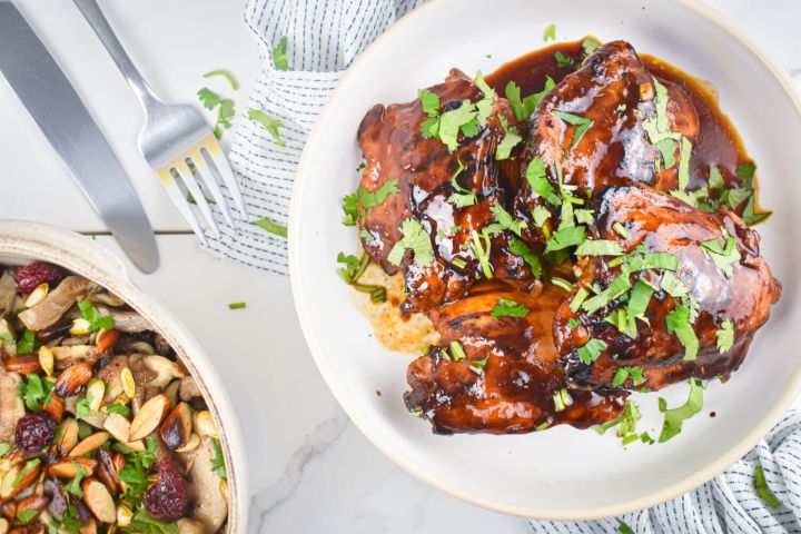 Broiled spicy barbecue chicken thighs on a plate with cilantro and a salad on the side.