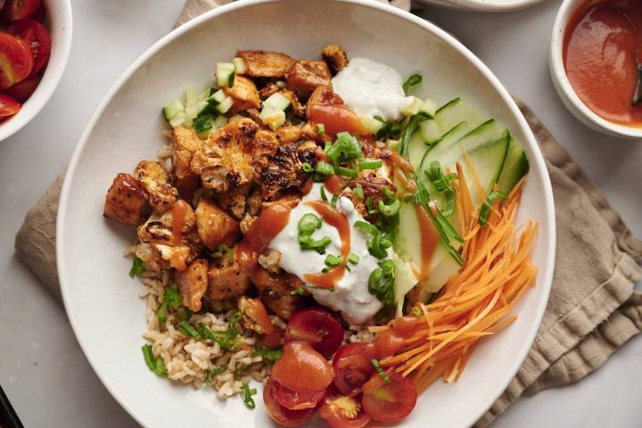 Buffalo chicken bowls with cauliflower, rice, carrots, cucumber, cherry tomatoes, buffalo sauce, and blue cheese dressing.