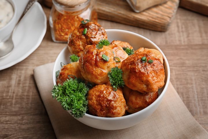 Slow cooker buffalo chicken quinoa meatballs on a plate covered in orange buffalo sauce.