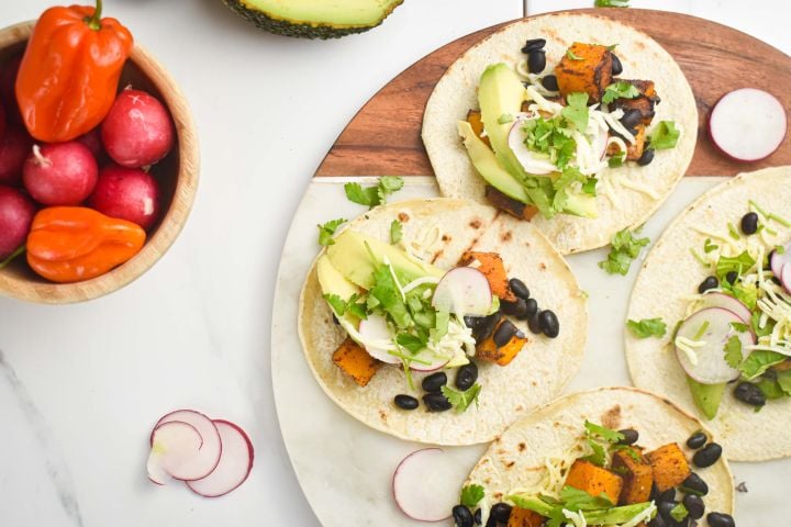 Butternut squash black bean tacos on corn tortillas with cilantro, cheese, avocado, and onions.
