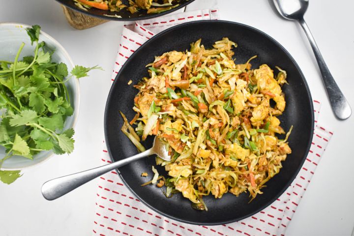 Cabbage fried rice with shredded cabbage, carrots, green onions, eggs, and soy sauce on a black plate.