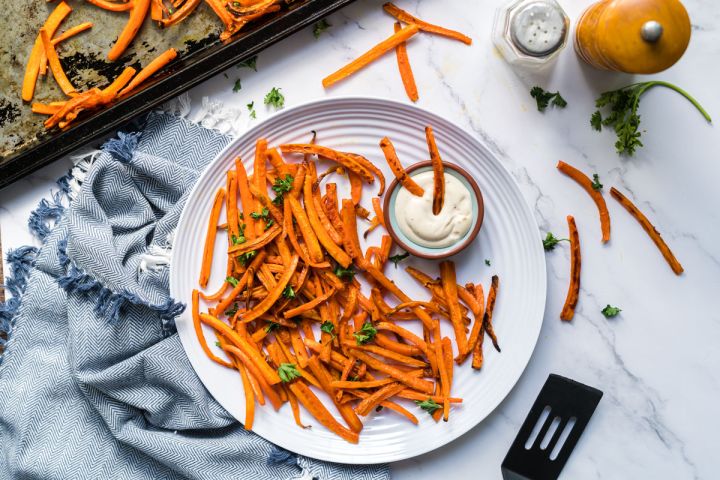 Carrot fries baked until crispy served on a plate with ranch dressing for dipping.