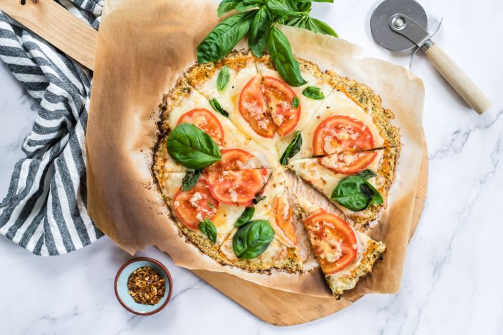 Cauliflower crust pizza made with cauliflower florets and topped with mozzarella cheese, tomatoes, and basil for a low carb pizza.