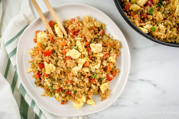 Cauliflower fried rice with cabbage, carrots, eggs, and green onions on a plate with chopsticks.