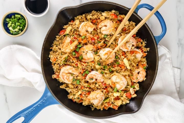 Cauliflower shrimp fried rice with cabbage, carrots, green onions, and soy sauce in a skillet.