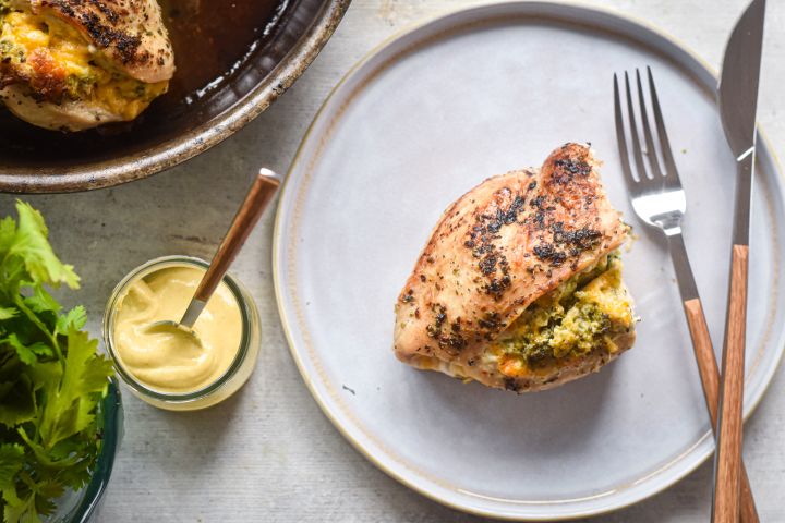 Stuffed chicken breasts with broccoli and cheddar on a plate with mustard on the side.