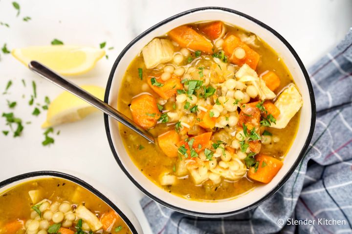 Chicken sweet potato soup with Israeli couscous in a bowl with lemon and parsley.