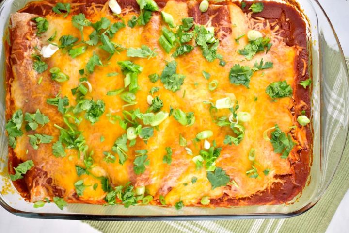 Chicken and bean enchiladas in a casserole dish with melted cheese on top.