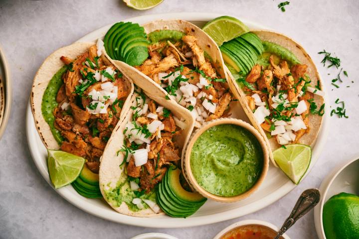 Chicken carnitas tacos with fresh cilantro, diced white onion, avocado, and salsa verde in corn tortillas.