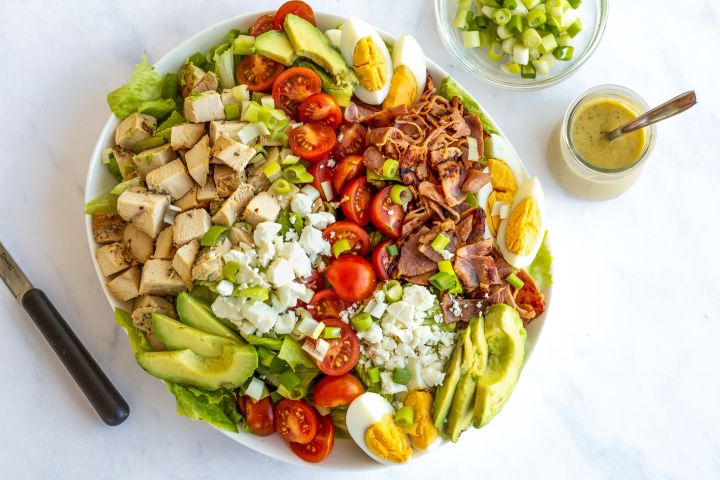 Chicken cobb salad with lettuce, grilled chicken, boiled eggs, bacon, tomatoes, and blue cheese.