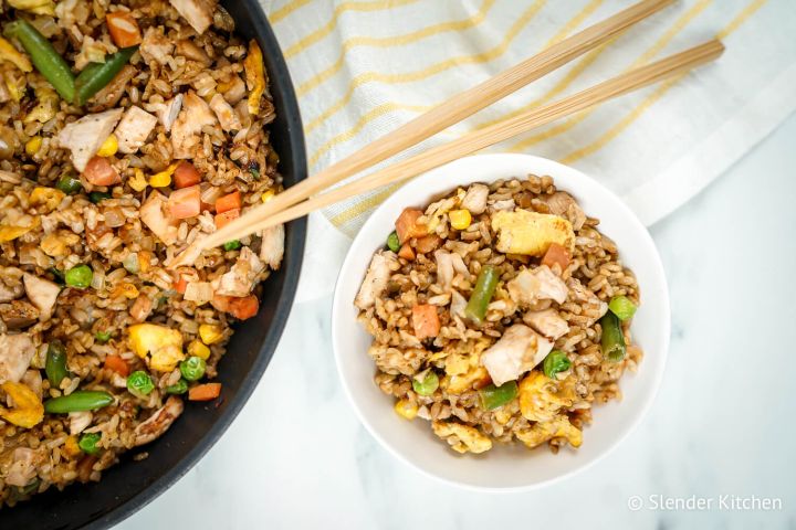 Chicken fried rice in a bowl with eggs, peas, carrots, chicken, and green beans with chopsticks.