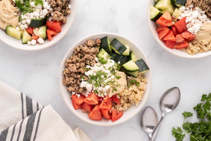 Chicken kofta bowls with tomatoes, cucumbers, hummus, and feta cheese in a bowl.