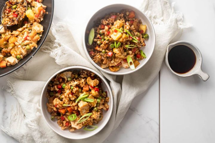 Chicken pineapple fried rice served in two bowls with fresh pineapple, chicken breast, brown rice, and vegetables with cashews.