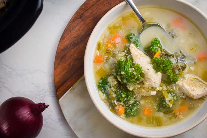 Slow cooker chicken quinoa soup with kale, carrots, celery, and onions in a bowl with a spoon.