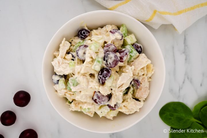 Chicken salad with grapes, celery, and yogurt dressing in a bowl with grapes and spinach on the side.