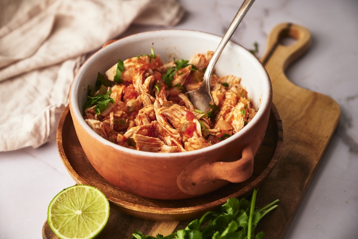 Chicken tinga in a bowl with onions, cilantro, avocado, and queso fresco.