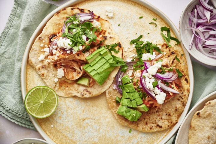 Chicken tinga tacos served on corn tortillas with queso fresco, cilantro, lime, and red onion.