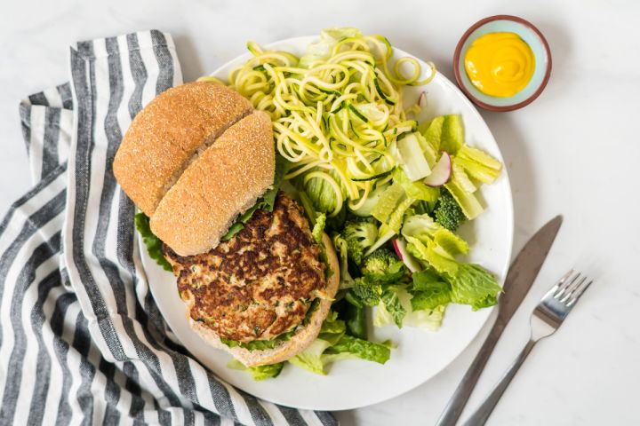 Chicken zucchini burgers on a plate with fresh herbs and ricotta cheese.