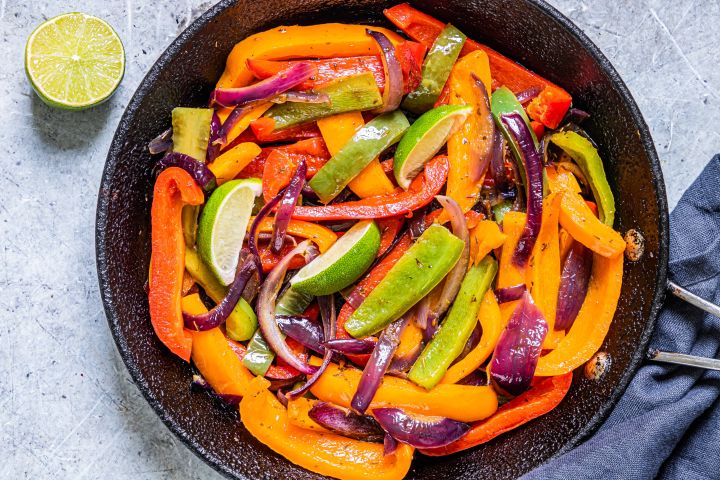 Chipotle fajita veggies with bell peppers and red onions in a skillet with lime wedges. 