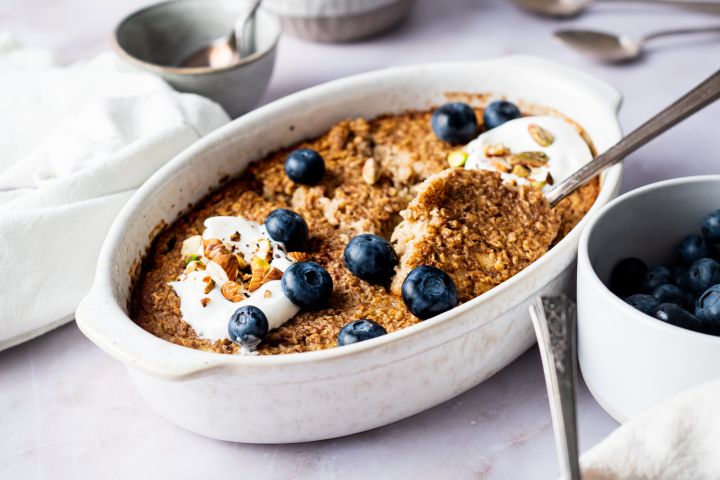Cinnamon baked oatmeal with rolled oats baked in a white dish topped with blueberries and honey.