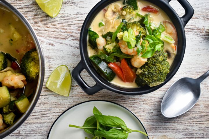 Coconut curry shrimp in a bowl with fresh vegetables, basil, green onions, and lime.