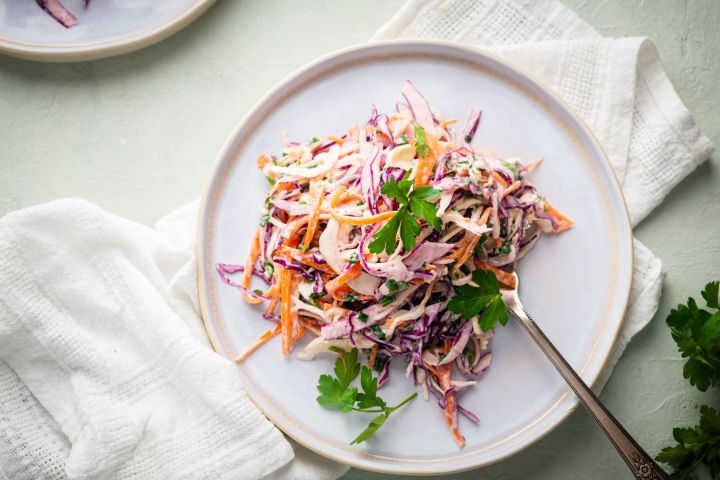 Coleslaw with shredded purple cabbage, green cabbage, carrots, and cilantro on a white plate.