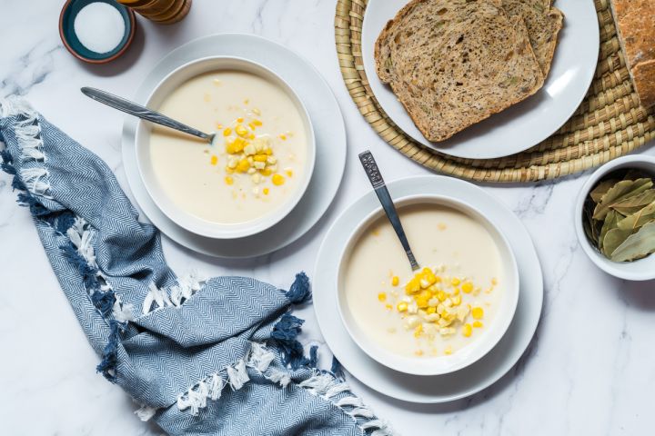 Corn chowder made with fresh corn, cauliflower, onions, milk, and spices in two bowls with bread on the side.