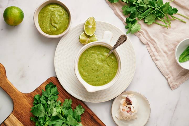 Creamy avocado salsa verde with avocados and tomatillos served in a white dish with cilantro and garlic on the side.