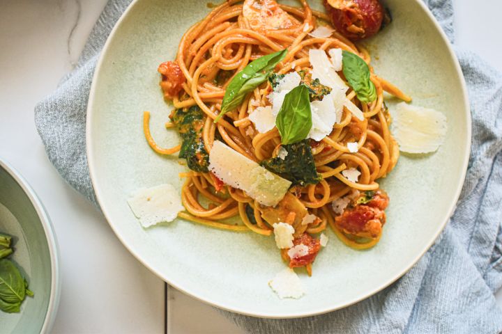 Creamy tomato mushroom and spinach pasta on a plate with whole grain pasta, creamy sauce, spinach, mushrooms, and parmesan cheese.