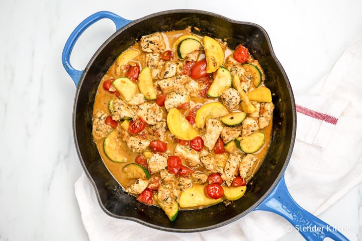 Healthy Tuscan chicken in a skillet with tomatoes, zucchini, and summer squash.