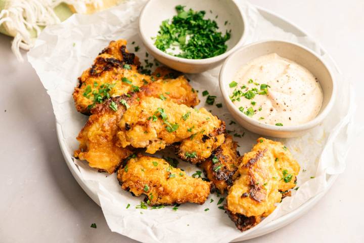 Golden brown buttermilk chicken tenders garnished with chopped parsley and served with a creamy seasoned dipping sauce.