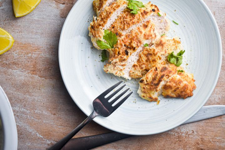 Buttermilk chicken breast cooked until crispy and sliced on a plate with lemon.