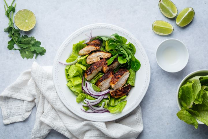 Cumin chicken breast with a homemade spice rub that's sliced and served with lime and salad greens.