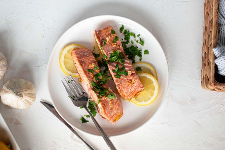 Dijon baked salmon with a garlic, lemon, and Dijon mustard sauce on a plate with garlic on the side.