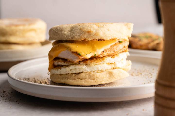 A breakfast sandwich on a plate, featuring a fluffy English muffin, melted cheese, chicken, and egg, conveying a warm, appetizing feel.