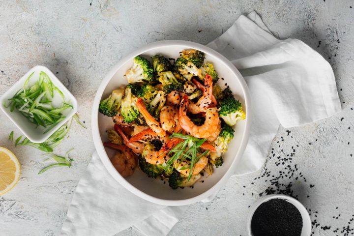 Firecracker shrimp and broccoli in a bowl with green onions and sesame seeds.