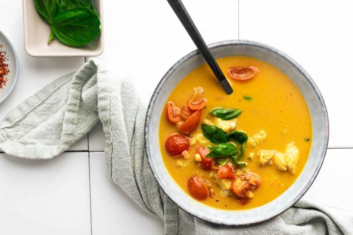 Fish curry with cooked cod, coconut broth, curry seasoning, garlic, ginger, and basil in a bowl with tomatoes. 