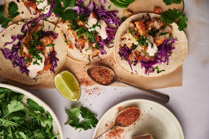 Fish taco seasoning served on a spoon and served with fish tacos, cabbage slaw, cilantro, and taco sauce. 