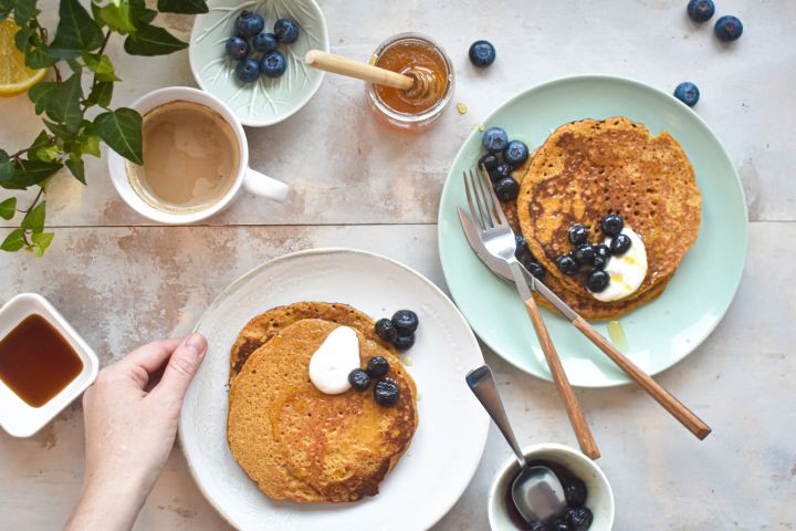 Low carb Flaxseed meal pancakes stacked on a plate with berries, yogurt, and a drizzle of syrup.