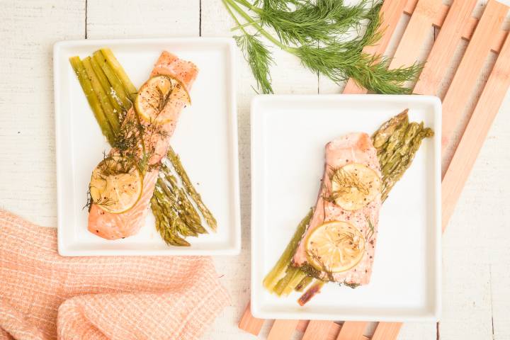 Foil baked salmon with asparagus, lemon, and dill on two plates.
