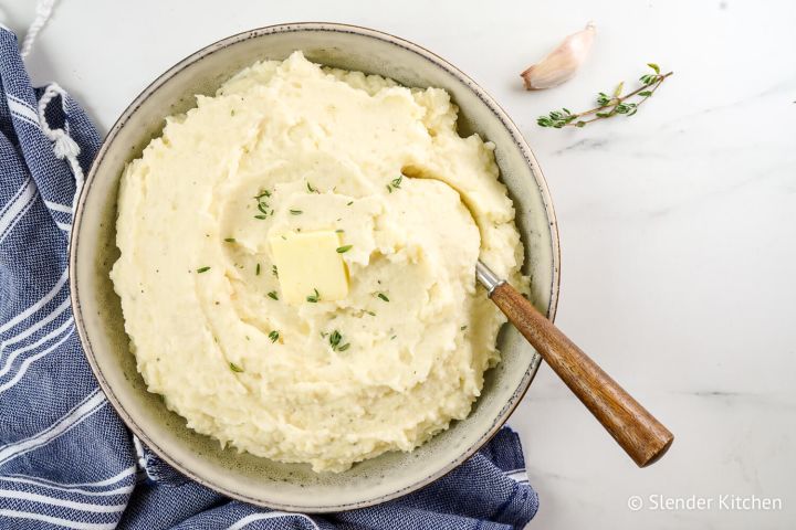 Cauliflower potato mash with roasted garlic and butter in a ceramic bowl with a wooden spoon.