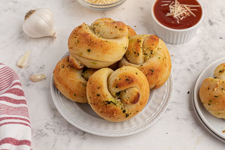 Garlic knots made with two ingredient dough topped with fresh garlic, melted butter, and basil on a plate with marinara sauce on the side.