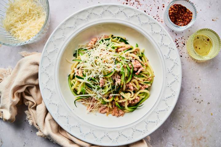 Garlic parmesan zucchini noodles with ground sausage and red pepper flakes in a white bowl.