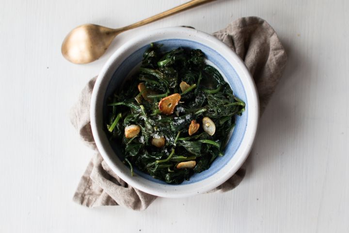 Garlic sautéed spinach with crispy garlic, black pepper, lemon, and sea salt on a white plate. 