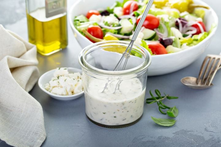 Greek salad dressing in a jar with feta cheese on the side.