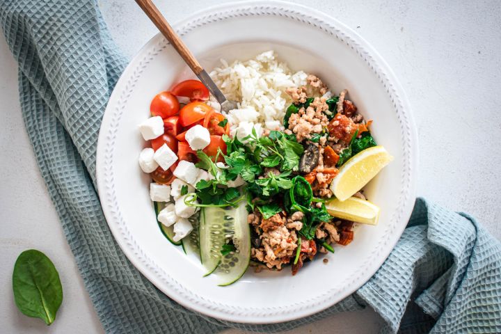 Greek groudn turkey served in a bowl with cherry tomatoes, feta cheese, cucumbers, and fresh herbs. 