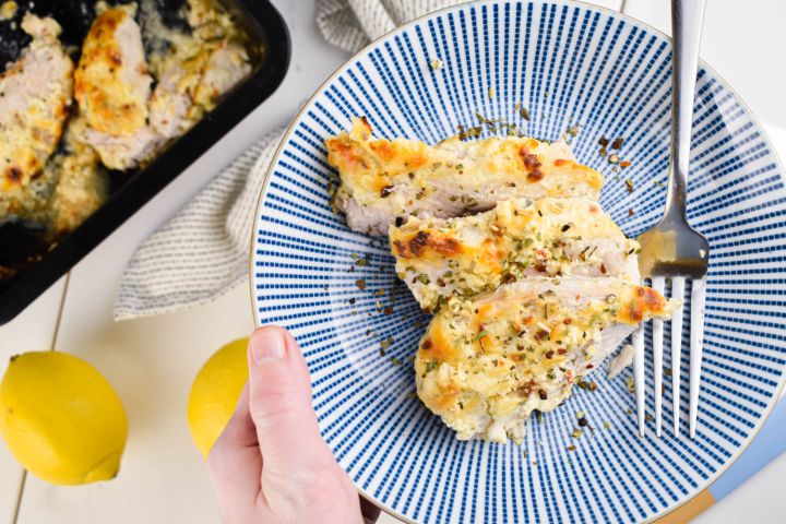 Baked Greek Yogurt Parmesan Chicken with herbs, lemon juice, Parmesan cheese, and garlic on a blue plate.